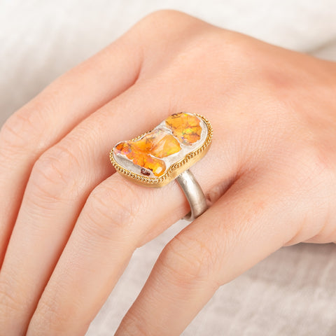A close up of a person wearing a handcrafted one-of-a-kind ring with a mexican opal gemstone, 18k gold bezel and sterling silver band