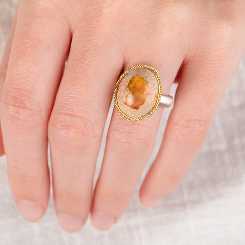 Hand wearing a mexican opal ring set with a handcrafted 18k gold bezel and sterling silver band