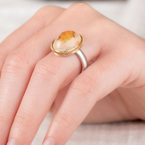 Hand wearing a mexican opal ring set with a handcrafted 18k gold bezel and sterling silver band