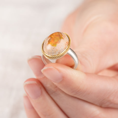 Hand holding a mexican opal ring set with a handcrafted 18k gold bezel and sterling silver band