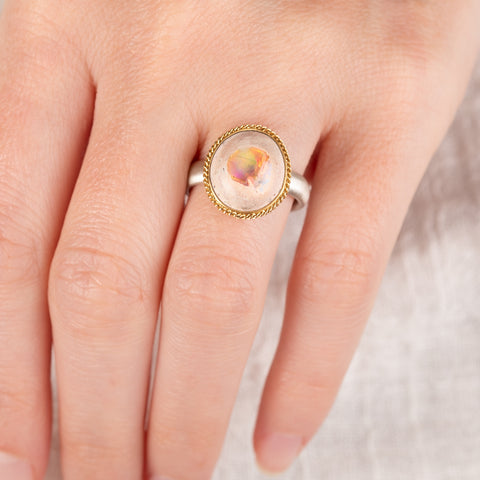 Close-up of a hand wearing a ring with a mexican opal gemstone set in an 18k gold bezel with a sterling silver band