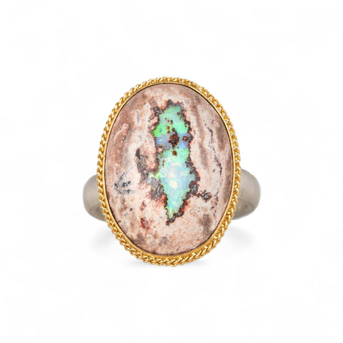 Handcrafted ring with a mexican opal stone, gold setting and sterling silver band on a white background.