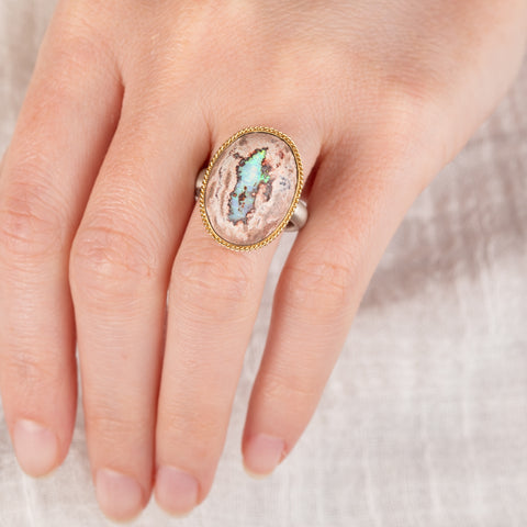 Close-up of a hand wearing a silver and gold ring with a mexican opal stone