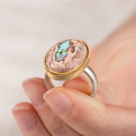 Mexican opal ring with a gold bezel and sterling silver band held by a hand on a light background