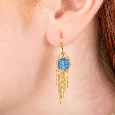 Gold earrings featuring carved moonstones, shown worn in a person's ear.