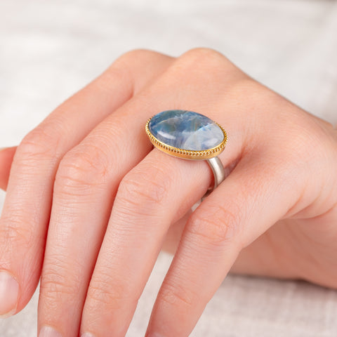 A hand wears a handmade gold and silver ring with a Moonstone gemstone
