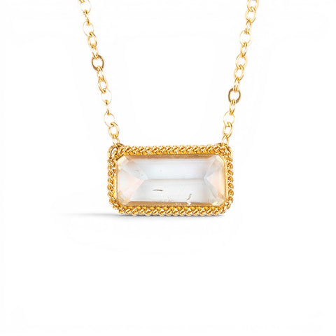 A gold necklace featuring a moonstone gem, against a white background.