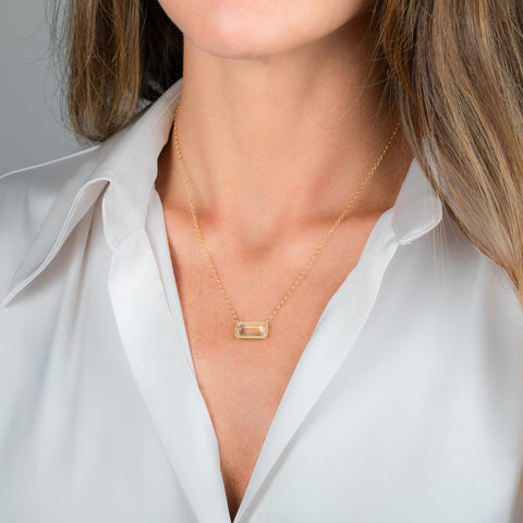A gold necklace featuring a moonstone gem, worn on a person's neck.