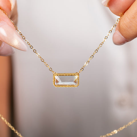 A close up of a gold necklace featuring a moonstone gem held in hand.