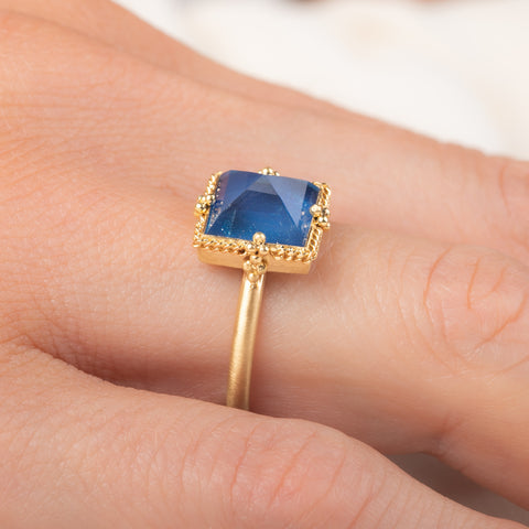 A gold ring featuring a blue moonstone gemstone, worn on a finger.