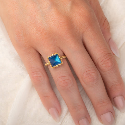 A gold ring featuring a blue moonstone gemstone, worn on a finger.