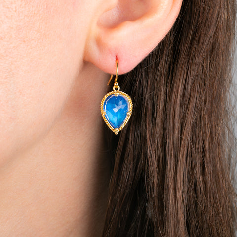 A close-up of a person's ear wearing a gold earring with a moonstone.