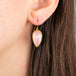 A gold drop earring featuring a pink morganite gemstone in a textured gold bezel setting, shown worn in a person's ear.
