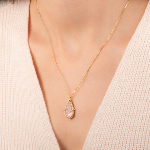 Teardrop-shaped morganite necklace set in an 18k gold bezel and matching chain, worn on a person's neck.