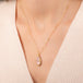 Teardrop-shaped morganite necklace set in an 18k gold bezel and matching chain, worn on a person's neck.