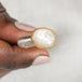 Gold and silver ring with a mother of pearl held in a person's hand against a neutral background