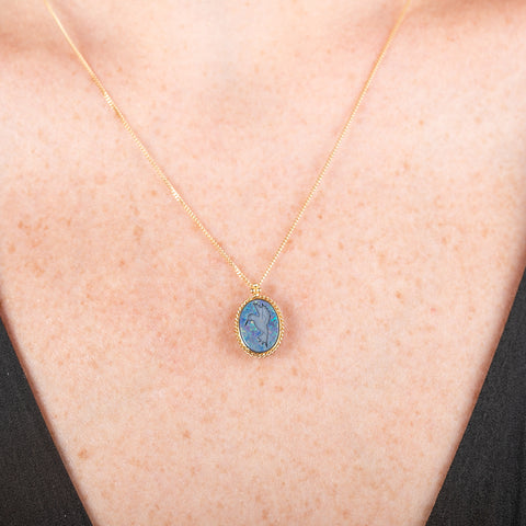 Handmade 18k yellow gold necklace featuring an opal doublet with a carved hummingbird worn by a person
