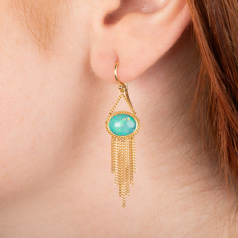 Gold earrings featuring Ethiopian opal gemstones with gold chain tassels, shown worn on a person's ear.