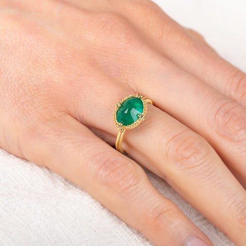 Gold ring with an emerald gemstone on a hand against a white background
