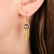 A pair of gold dangle earrings with oval diamond gemstones and cascading gold chain fringe, show worn on a model's ear.