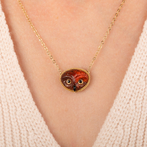 Gold necklace featuring a carved owl pendant made from garnet with an onyx beak, worn on a person's neck.