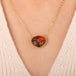 Gold necklace featuring a carved owl pendant made from garnet with an onyx beak, worn on a person's neck.