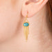 Gold earrings featuring paraiba kyanite gemstones and gold chain tassels, shown worn in a person's ear.