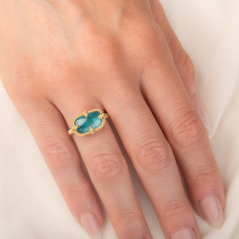 Gold ring featuring a teal pariba kyanite stone set in an 18k gold bezel, worn on a person'd finger.