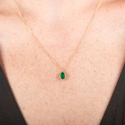 Gold necklace with a petite emerald gemstone set in a handmade gold bezel on a person's neck.