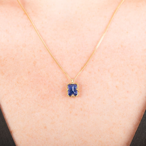 Gold necklace with a tanzanite gemstone set in a handmade gold bezel on a person