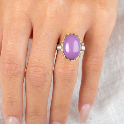 A gold and silver ring with a purple phosphosiderite stone, worn on a person's hand.