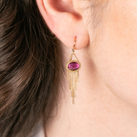 Gold earrings with pink tourmaline gemstones worn by a person