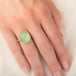 A gold ring featuring a prehnite with a fairy design carved in it, worn on a person's finger.