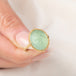 A gold ring featuring a prehnite with a fairy design carved in it, held in hand.