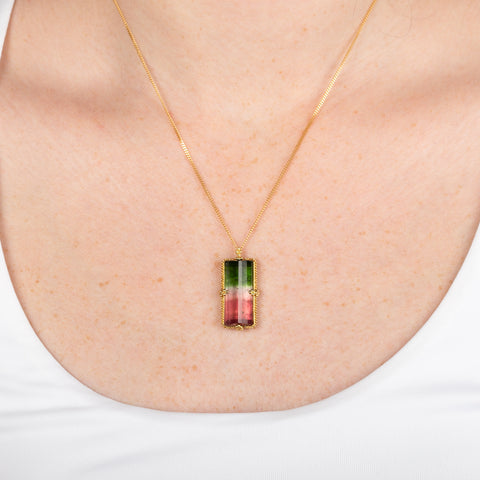 Watermelon tourmaline gemstone necklace with a gold setting worn on a person