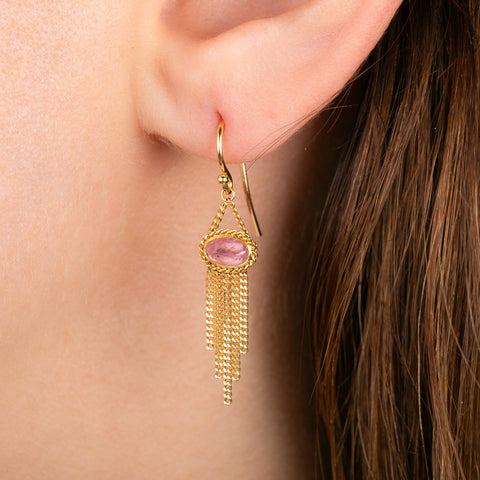 A gold dangle earring with oval pink rhodochrosite gemstones and cascading gold chain fringe, shown worn on a model's ear.