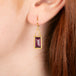 Gold earrings featuring rhodolite garnet gemstones shown worn in a person's ear.