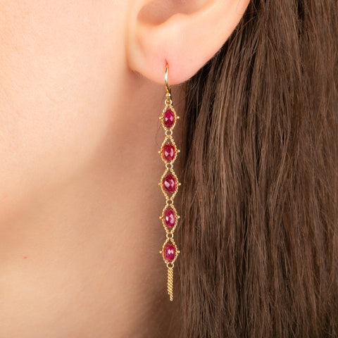 Gold earrings featuring a row of five ruby stones, worn on a person's ear.