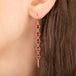 Gold earrings featuring a row of five ruby stones, worn on a person's ear.