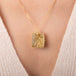 A gold pendant necklace featuring a rutilated quartz gemstone filled with fine metallic gold needles, worn on a person's neck.