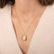 A gold pendant necklace featuring a rutilated quartz gemstone filled with fine metallic gold needles, worn on a person's neck.