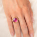 Gold and silver ring featuring a bright pink sapphire gemstone, worn on a person's finger.