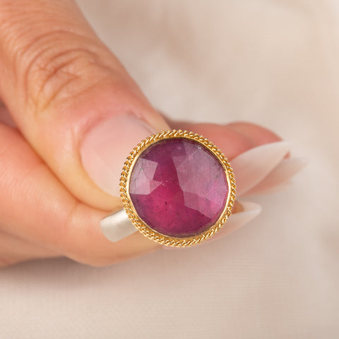 Gold and silver ring featuring a bright pink sapphire gemstone, held in hand.