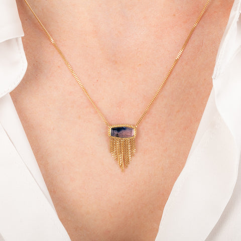 Gold necklace with a ruby sapphire gemstone pendant on a person