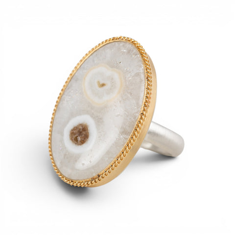An oval ring featuring a solar quartz stone set in a textured gold bezel with a sterling silver band, shown against a white background.