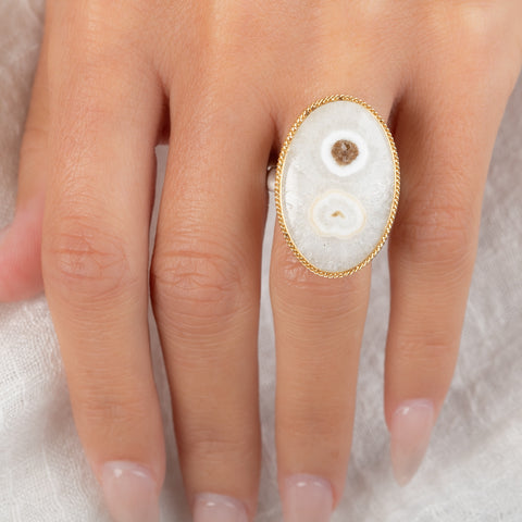 An oval ring featuring a solar quartz stone set in a textured gold bezel with a sterling silver band, worn on a person's finger.