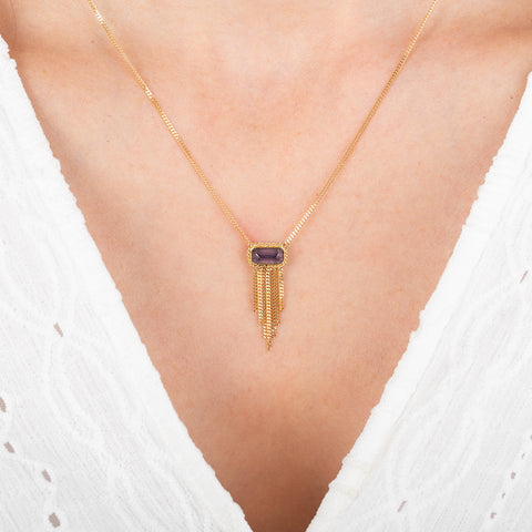 Gold necklace with a a spessartite gemstone adorned with a gold tassel on a person wearing a white top.