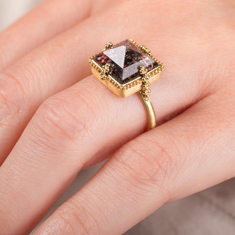 A photo that shows the close up details of a handcrafted 18k gold and super 7 gemstone ring.