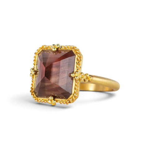 A gold ring featuring an Oregon Sunstone gemstone in a 18k gold bezel setting, shown against a plain white background.