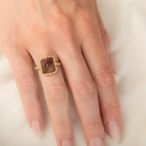 A gold ring featuring an Oregon Sunstone gemstone in a 18k gold bezel setting, worn on a person's finger.